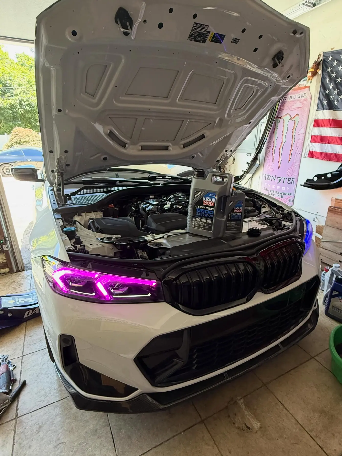 White BMW 3 Series with purple DRLs lit, hood open with Liqui Moly Top Tec 6600 oil on the engine