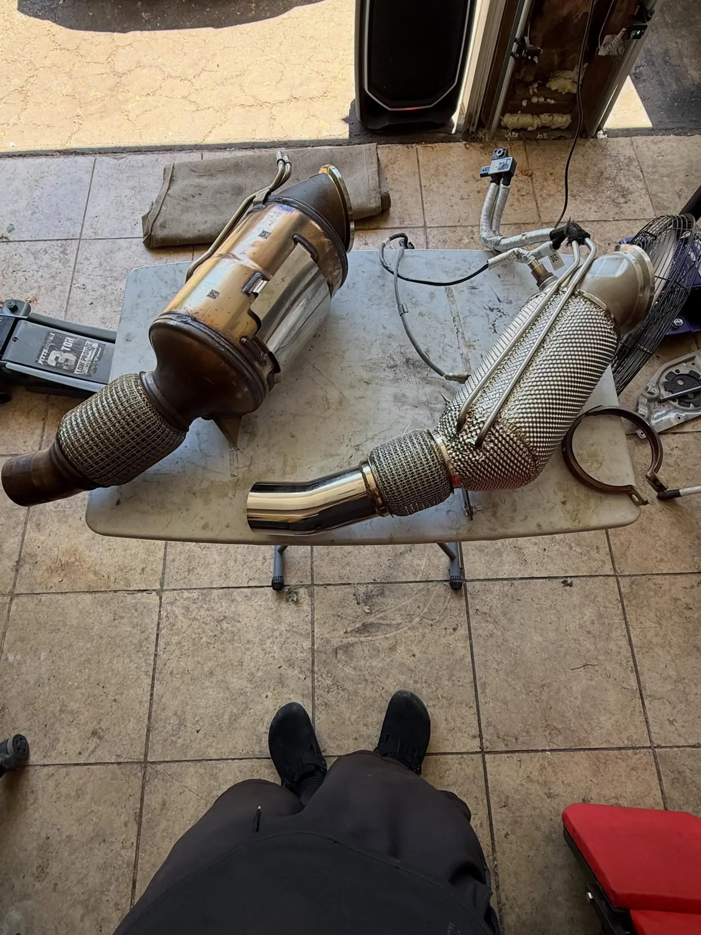 Stock downpipe next to the new heat-wrapped downpipe on a table in the garage